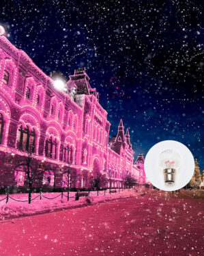 En historisk bygning oplyst af pink LED-lys i vinterlandskab med sne og faldende snefnug. I hjørnet ses en LED-pære med B22-fatning og lyserøde dioder.