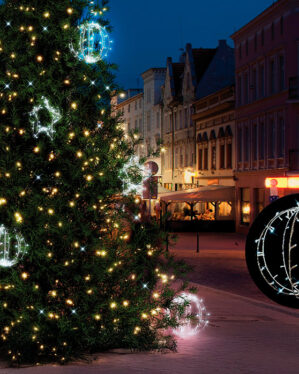 Juletræ på bytorv pyntet med varme og kolde LED-lys og kugleformede dekorationer, der lyser op i vinteraftenen med festlig stemning.