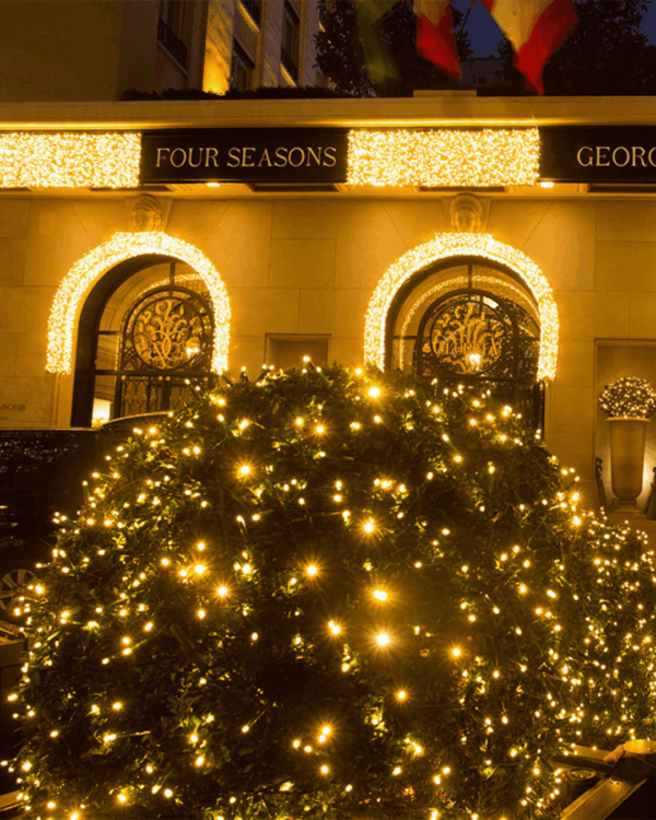 Indgang til Four Seasons George med buede porte og buske dækket af små gule lys - elegant og festlig belysning.