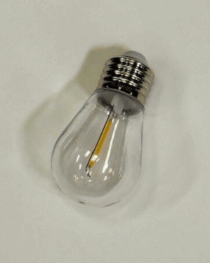 En varm hvid LED-pære med klar glas og E27 fatning, liggende på hvid overflade. Velegnet til udendørs festoon-lyskæder og energieffektiv stemningsbelysning i professionel kvalitet.