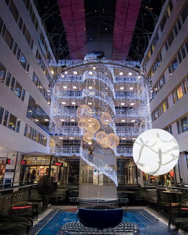 Indendørs centerudsmykning med hvide LED-lysgardiner og gyldne kuglemotiver i flere etager. Nærbillede viser energieffektive LED på hvid ledning, perfekt til professionel julebelysning.