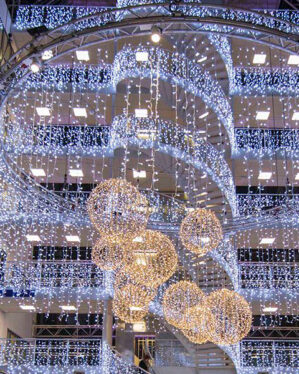Imponerende indendørs juleudsmykning med hængende LED-lysgardiner i kold hvid og dekorative lysende kugler, der skaber et eksklusivt, festligt og elegant udtryk i shoppingcenter.