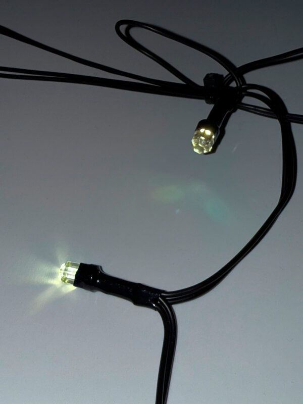 Nærbillede af varm hvid LED-pære på sort ledning, energivenlig istap lyskæde til juleudsmykning, skaber elegant lys med høj holdbarhed, velegnet ude og inde.