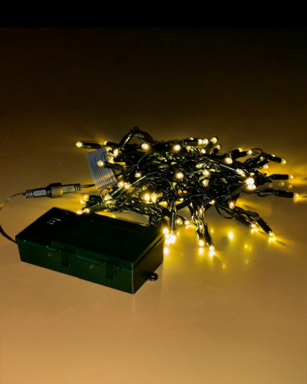 Batteridrevet LED-lyskæde med varm hvid belysning og sort kabel, forbundet til grøn batteriboks. Perfekt til fleksibel og dekorativ indendørs eller udendørs juleudsmykning året rundt.