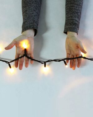 Person viser en sort LED-lyskæde med varm hvid belysning mellem hænderne, demonstrerer fleksibilitet og lysstyrke til professionel juleudsmykning og dekorativ anvendelse.