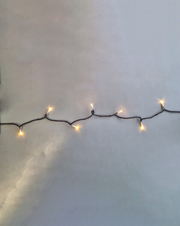 Sort LED-lyskæde med varm hvid belysning monteret på væg. Viser jævn lysfordeling og høj kvalitet, ideel til professionel indendørs juleudsmykning.