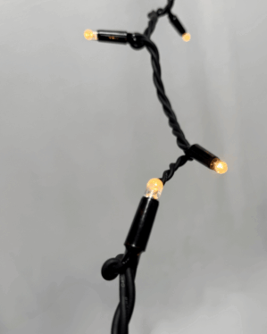 Nærbillede af sort stinglight med små, varmt hvide dioder mod en lys baggrund. Fokus på pærernes glød og den snoede, robuste kabelkonstruktion.
