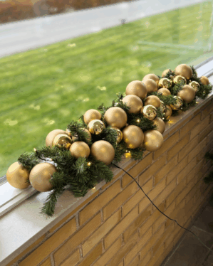Juleguirlande med matte og blanke guld julekugler samt små LED-lys. Placeret udendørs på vindueskant og giver et luksuriøst, varmt juleudtryk.