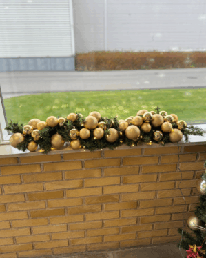 Elegant juleguirlande med matte og blanke guld julekugler samt varme LED-lys. Opsat på murstensvæg udendørs og skaber eksklusiv, stemningsfuld julepynt.