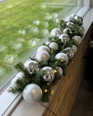 Juleguirlande pyntet med matte og blanke sølvkugler samt varme LED-lys. Opsat udendørs på vindueskant og giver et moderne, vinterligt udtryk.