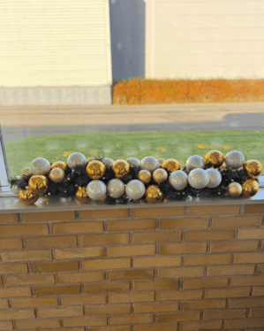 Pyntet juleguirlande med guld- og sølvkugler samt varme LED-lys. Elegant udsmykning placeret på vindueskant med et klassisk og luksuriøst juleudtryk.