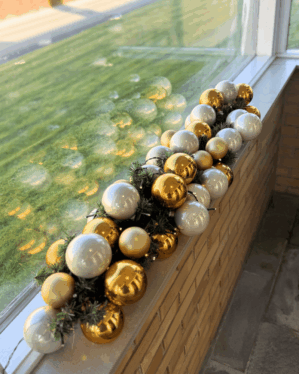 Juleguirlande med guld- og perlemor kugler samt LED-lys på vindueskarm. Skaber et elegant, moderne og festligt udtryk med reflekterende kugler og varm belysning.