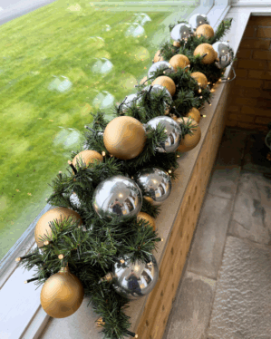 Pyntet granguirlande med kugler i sølv og guld samt varm hvid LED-lyskæde, der skaber et elegant og festligt udtryk i vindueskarmen.