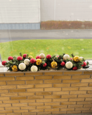 Granguirlande pyntet med røde, perlemor og guld kugler samt varm hvide LED-lys. Skaber en elegant og festlig julestemning i vindueskarmen.