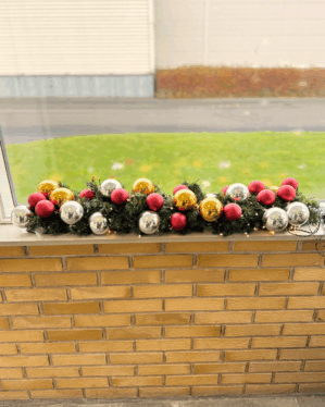 Pyntet granguirlande med røde, sølv- og guld kugler samt varm hvide LED-lys. Skaber en elegant og festlig julestemning i vindueskarmen.