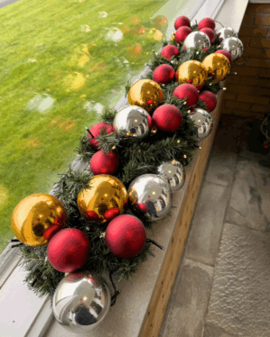 Elegant granguirlande pyntet med røde, guld og sølvfarvede kugler samt varm hvide LED-lys. Perfekt til vindueskarm eller butik for klassisk julestemning.