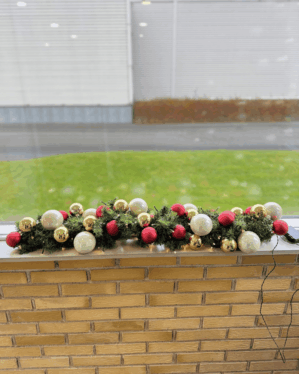 Pyntet granguirlande med røde, perlemor og champagne kugler samt varm hvide LED-lys. Skaber en stemningsfuld og elegant juledekoration i vindueskarmen.