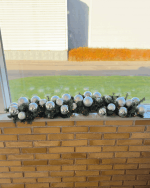 Juleguirlande med sølv og perlemor julekugler og varm LED-belysning placeret på vindueskarm. Elegant og moderne udsmykning, der skaber et stilrent og festligt vinterudtryk.