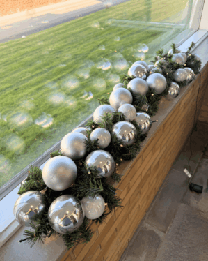Elegant juleguirlande med sølv og perlemor kugler og varm LED-belysning på vindueskarm. Skaber et moderne og festligt udtryk med blanke og matte overflader.