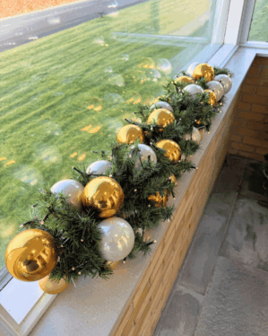 Elegant juleguirlande med grønne grene, perlemor og guldfarvede kugler samt varm LED-belysning. Perfekt til vindueskarm eller reception for et eksklusivt juleudtryk.