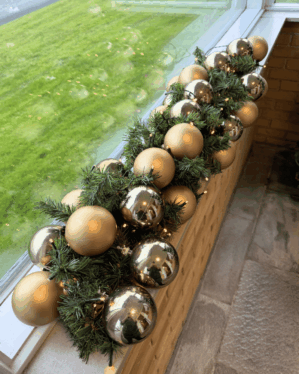 Elegant juleguirlande med champagne og sølv julekugler samt varm hvid LED-belysning. Placeret i vindueskarm og skaber en klassisk og luksuriøs julestemning.