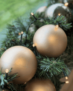 Detaljeret nærbillede af gyldne julekugler i champagne og sølv farve med en grøn guirlande med varm hvid LED-lys, der skaber et klassisk og elegant juleudtryk.