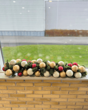 Granguirlande pyntet med perlemor, røde og champagne kugler i vindueskarm. Skaber et elegant, harmonisk og festligt juleudtryk med klassiske farver og let glans.