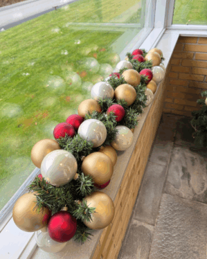 Elegant granguirlande pyntet med perlemor, røde og champagne kugler. Skaber et klassisk og harmonisk juleudtryk med flotte farver og dekorativ glans i vindueskarmen.
