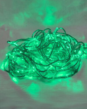 Grøn LED-lyskæde linelight ligger i en bunke på en lys overflade, mens det stærke grønne skær reflekteres på baggrunden og skaber en levende, dekorativ atmosfære.