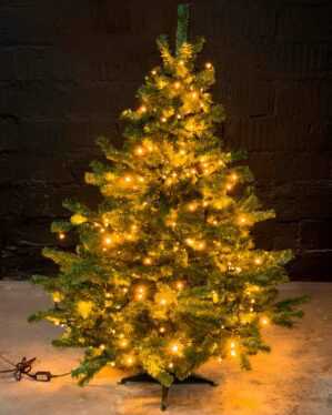 Kunstigt juletræ fra Exclusive-serien med tæt grøn struktur og integreret varm hvid LED-belysning, placeret indendørs på stabil sort fod, velegnet til stemningsfuld juledekoration i professionelle miljøer.