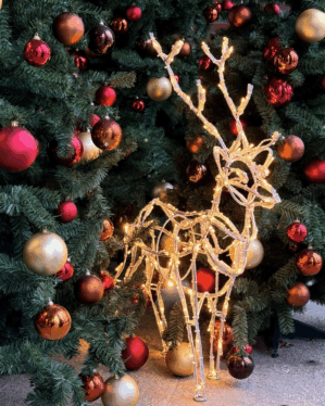 Mini stag juleudsmykning i aluminium med LED lyskæde der gemmer sig mellem nogle kunstige juletræer med julekugler.